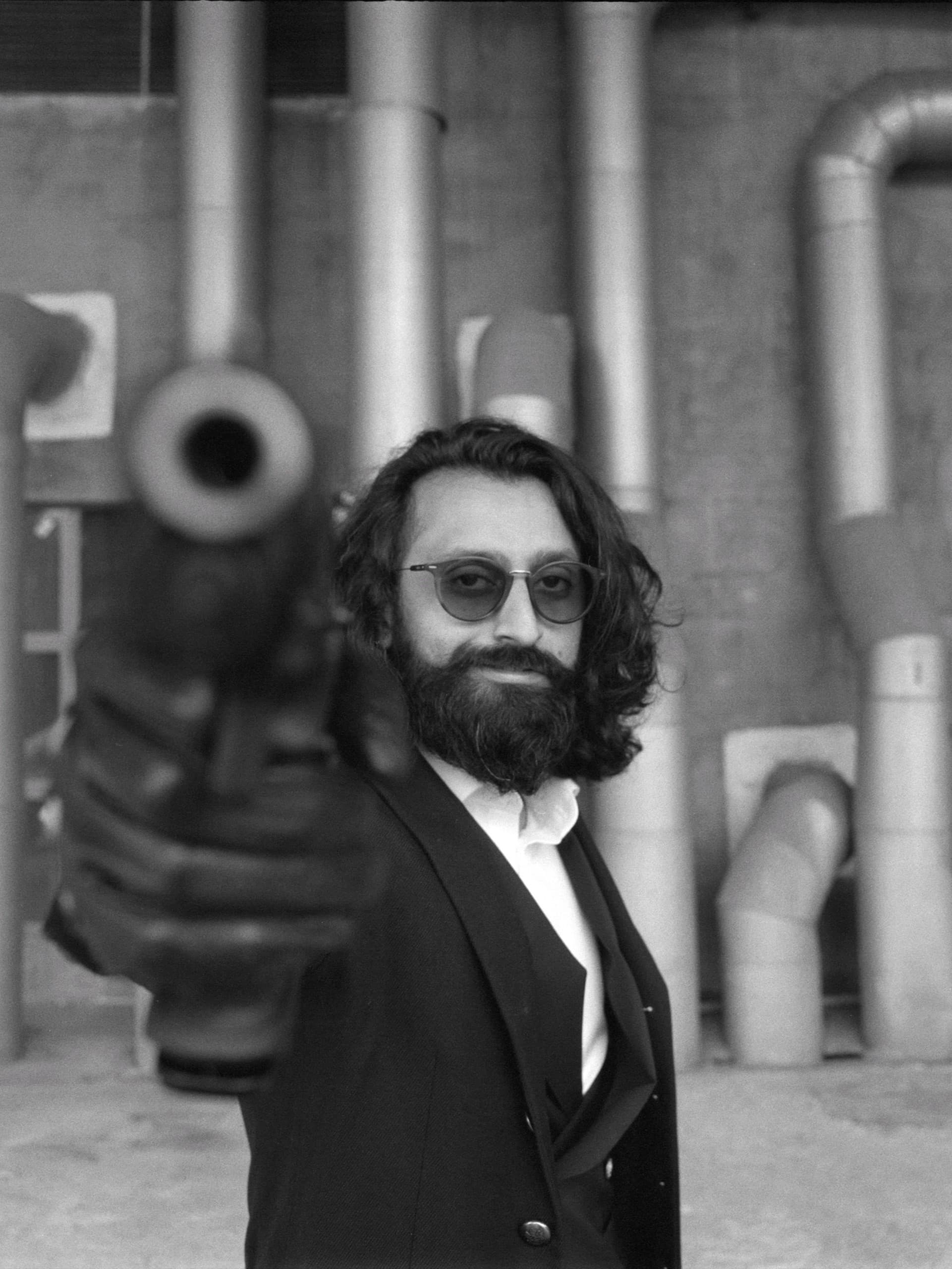 Cinematic black and white portrait of man with glasses pointing a gun at the camera on Ilford Delta 3200 film.