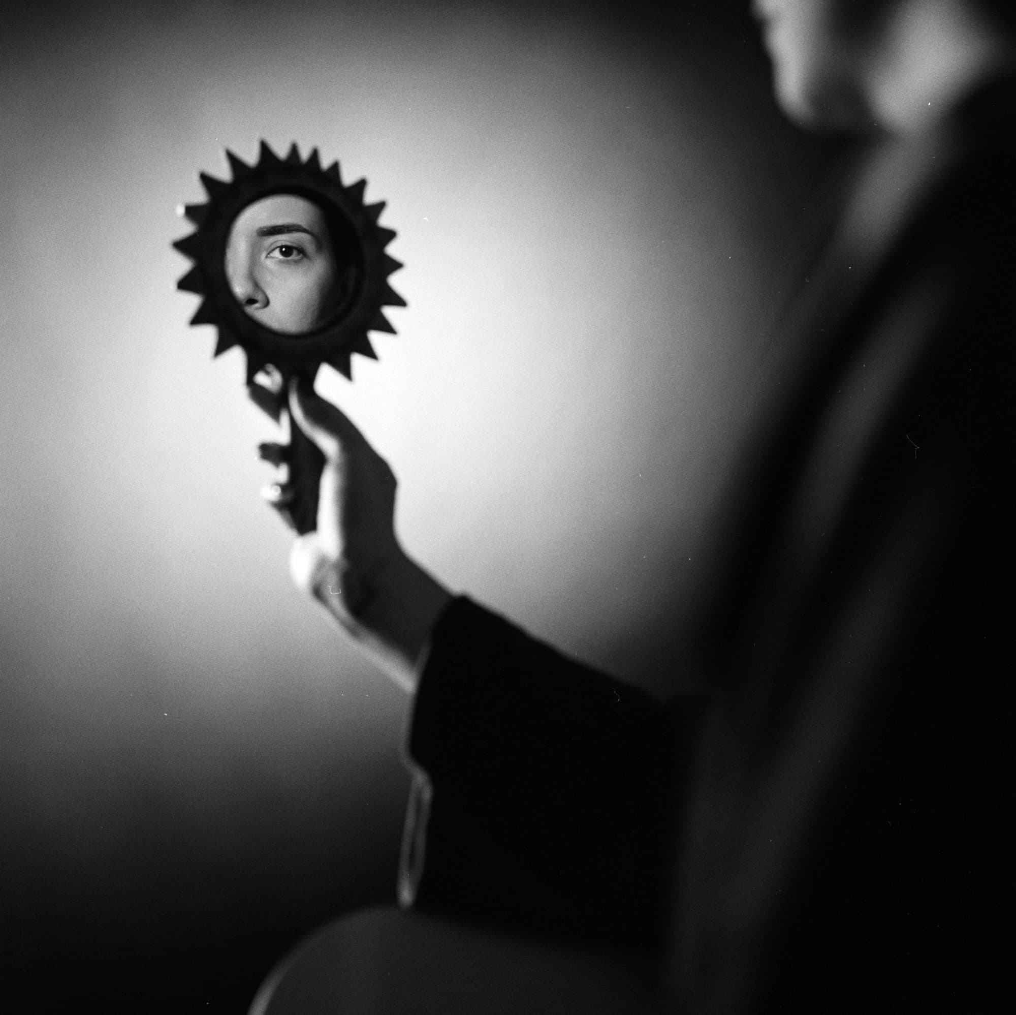 Creative black and white portrait with an eye framed in a handheld mirror on medium format Ilford HP5 film.