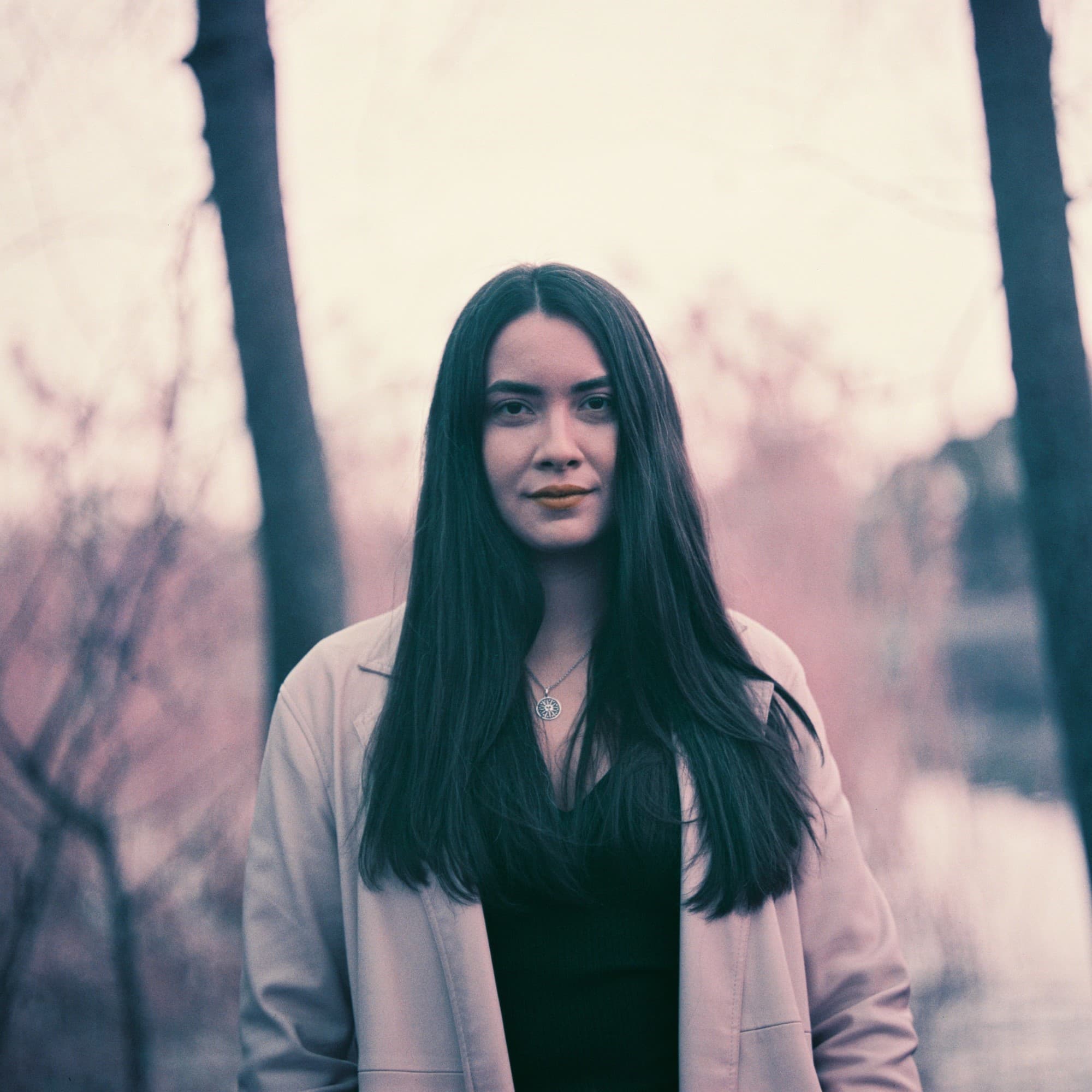 False color portrait of woman with long hair near the woods on Lomography Color Purple film.