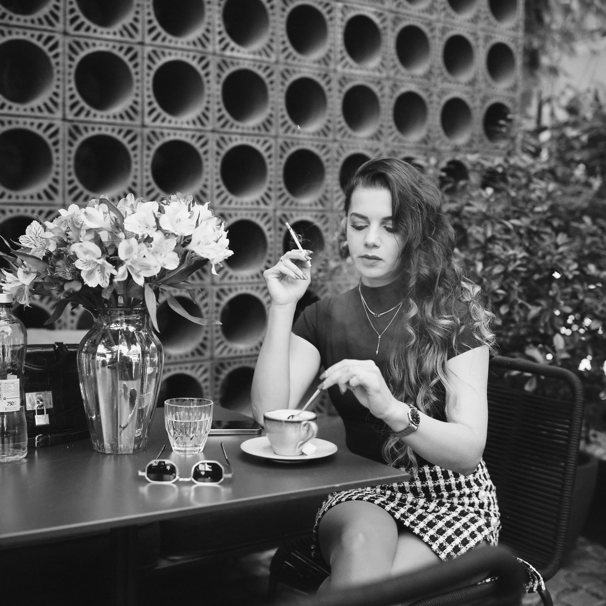 Portrait of fashionable woman enjoying her coffee outside on black and white Ilford XP2 film.