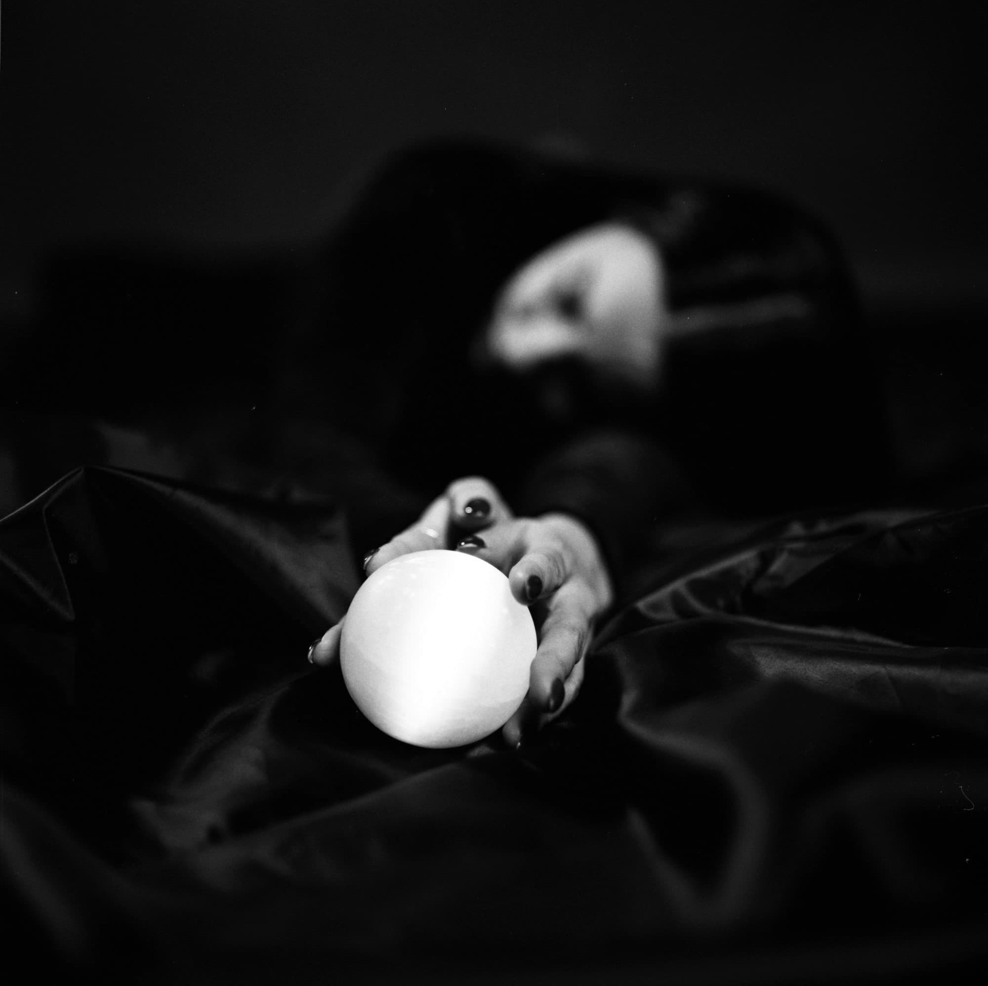 Black and white film portrait of a person holding a quartz sphere with shallow depth of field.
